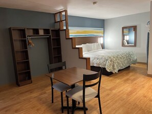 Un dormitorio con cama, escritorio, silla, armario y un cuadro en la pared.