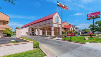 Red Roof Inn com telhado vermelho, bandeira do Texas e placa oferecendo café da manhã gratuito.