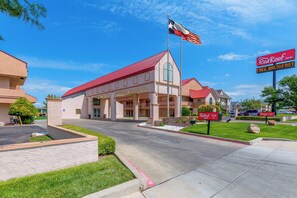 Un Red Roof Inn con techo rojo, una bandera de Texas y un letrero que ofrece desayuno gratuito.