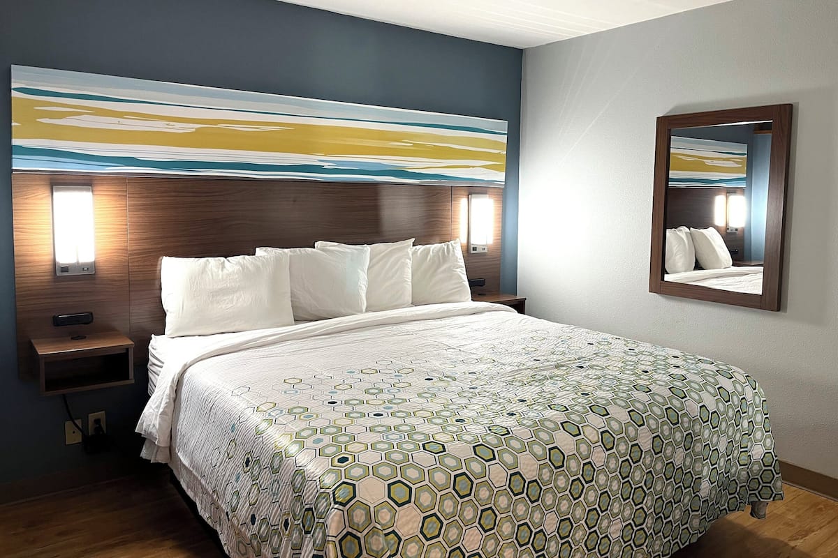 A hotel room with a large bed, a nightstand, a wall-mounted mirror, and a painting above the bed.