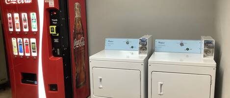 Een automaat met verschillende drankjes en een wasmachine van Whirlpool.