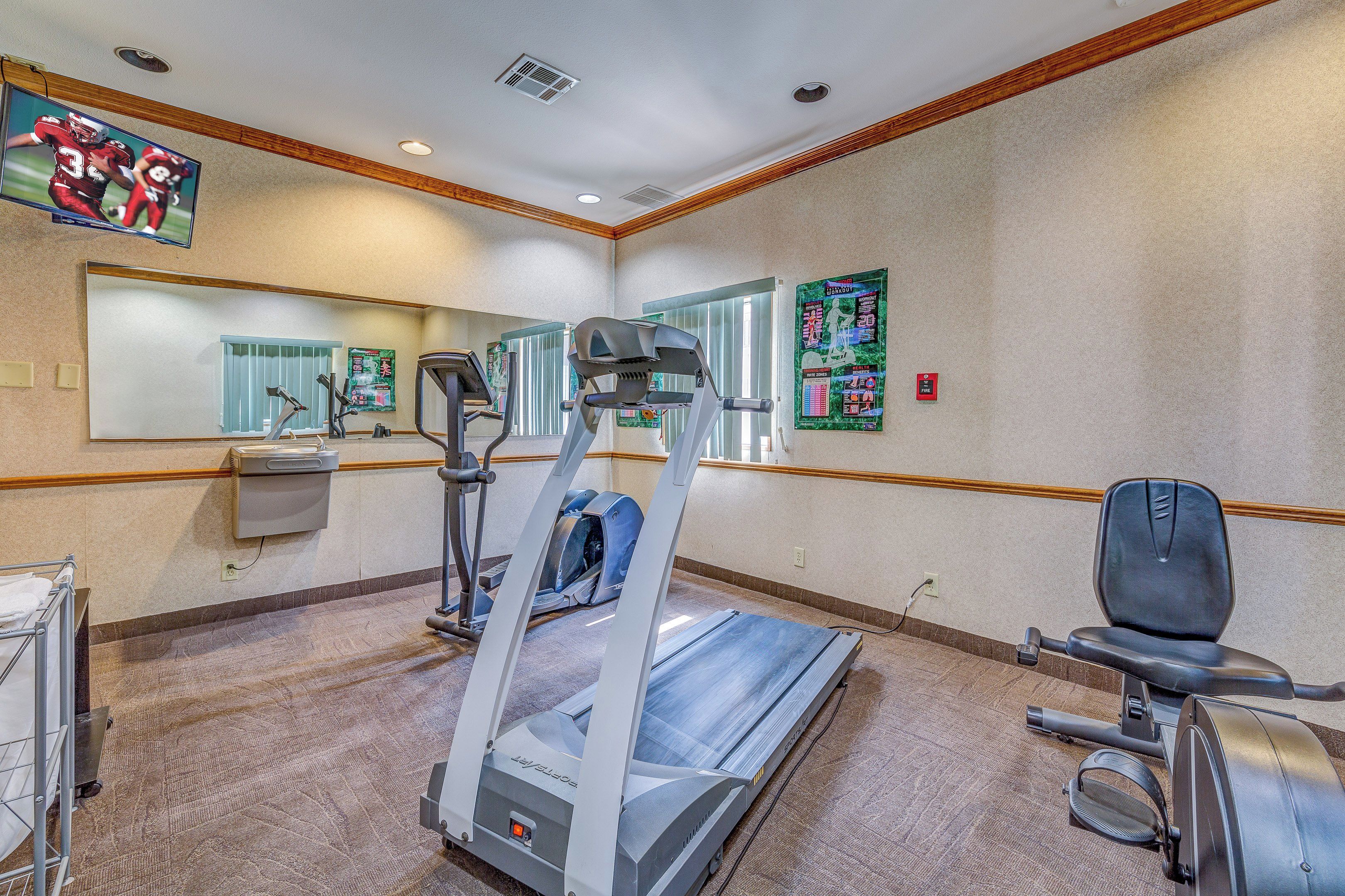 Une salle de remise en forme équipée de tapis de course, d’un vélo d’appartement et d’un mur recouvert de miroirs.