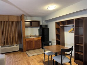 A compact kitchen with a dining table and chairs, a built-in microwave, and a refrigerator.