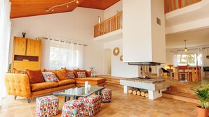 A spacious living area with a wooden ceiling, a sofa set, a coffee table, and a dining area with a wooden railing. - Grande Maison Familiale Avec Piscine Dans Quartier Résidentiel Calme (Langlade)