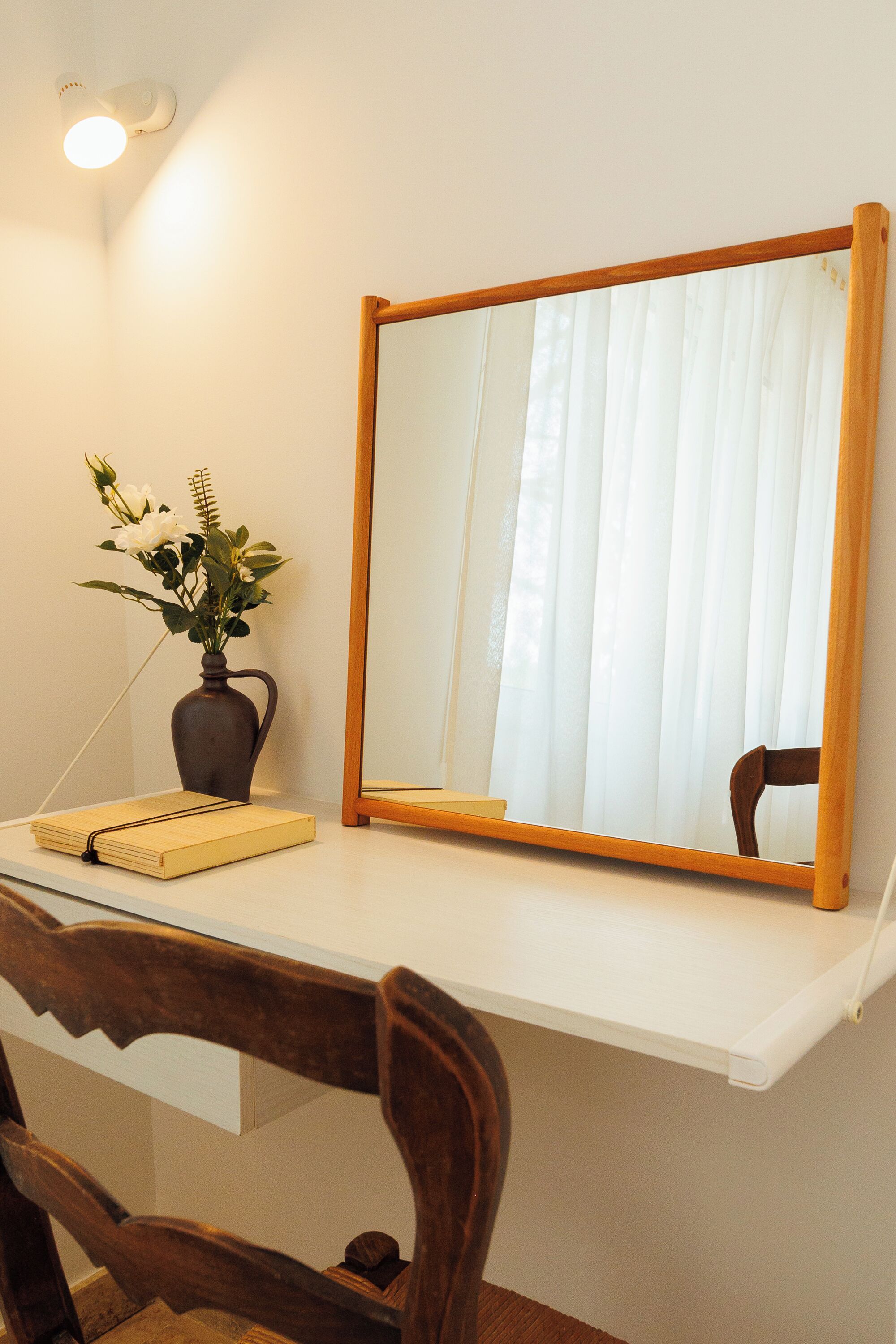 A desk with a mirror, a vase with flowers, and a chair.