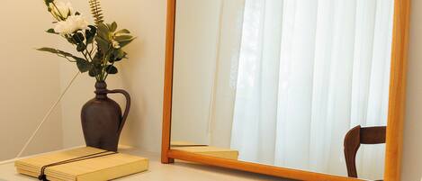 A desk with a mirror, a vase with flowers, and a chair.
