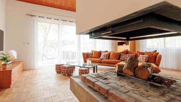 A living room with a brick fireplace, a sofa with patterned cushions, and a glass coffee table. - Grande Maison Familiale Avec Piscine Dans Quartier Résidentiel Calme (Langlade)