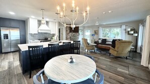 Een moderne keuken met een centraal eiland, een eethoek met een ronde tafel, en een zithoek met een bank en fauteuils.
