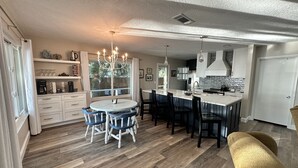 Een moderne keuken met een centraal eiland, witte keukenkastjes en een eethoek met blauwe stoelen.