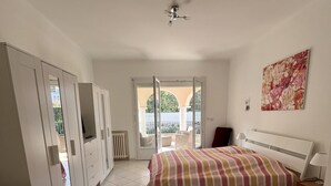 Un dormitorio con cama, escritorio, silla, ventilador de techo y vistas al balcón exterior.