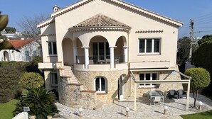 Una casa de dos pisos con fachada de piedra, una piscina y un patio con mobiliario exterior.