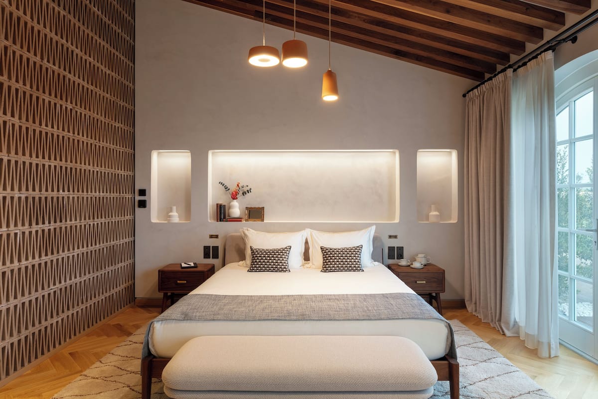 Un dormitorio moderno con una cama grande, mesitas de noche, una lámpara de pared y una ventana con cortinas.
