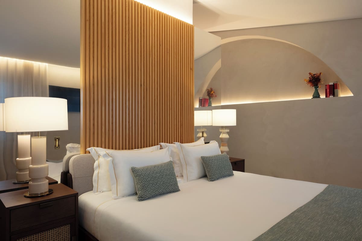 Una habitación de hotel moderna con una cama grande, mesitas de noche, lámparas y un panel decorativo en la pared.