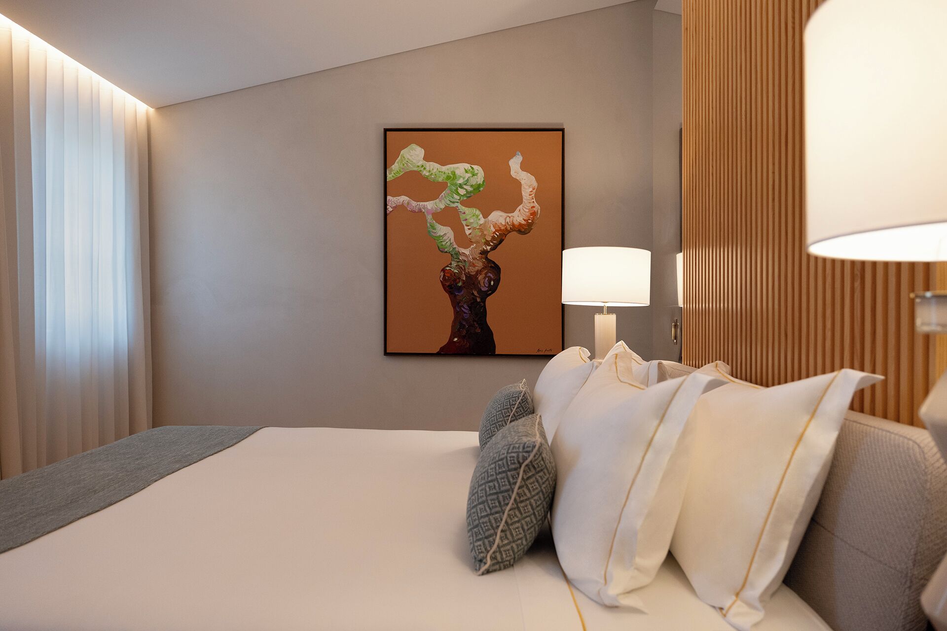 Een hotelkamer met een bed, kussens, een lamp en een schilderij aan de muur.