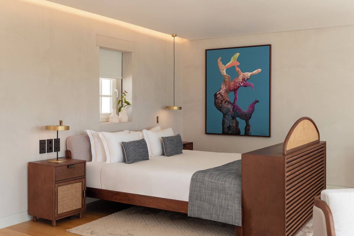 Un dormitorio moderno con cama, mesitas de noche, un espejo, una obra de arte en la pared y una lámpara de pie.