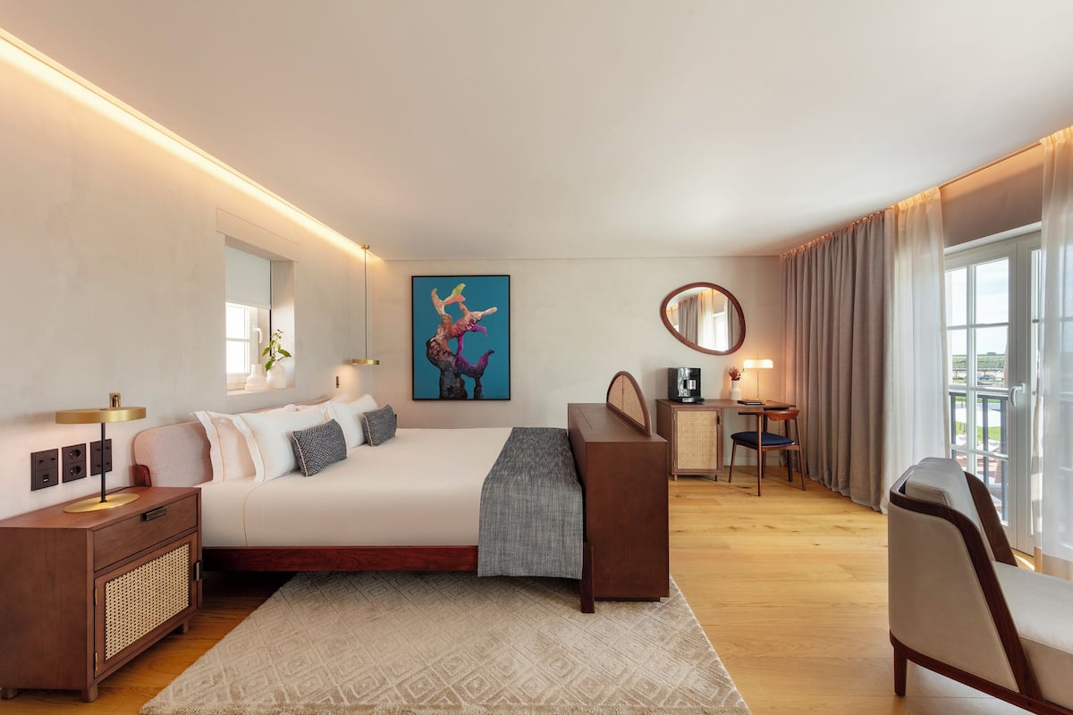 Una habitación de hotel moderna con una cama grande, mesitas de noche, un escritorio y vistas al exterior.