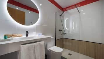 Une salle de bain moderne avec un lavabo blanc, un miroir rond, des toilettes et une douche à parois de verre.