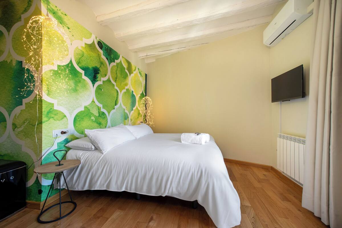 Un dormitorio con cama, mesita de noche, televisor de pared y equipo de aire acondicionado.