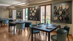 A dining area with multiple tables and chairs, a wall with various plates and utensils, and a view of the outside through large windows.