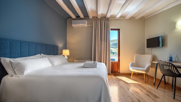 A hotel room with a large bed, a desk with a chair, a television, and a window with curtains.