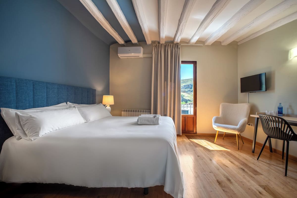 Habitación de hotel con una cama grande, un escritorio con una silla, un televisor y una ventana con cortinas.