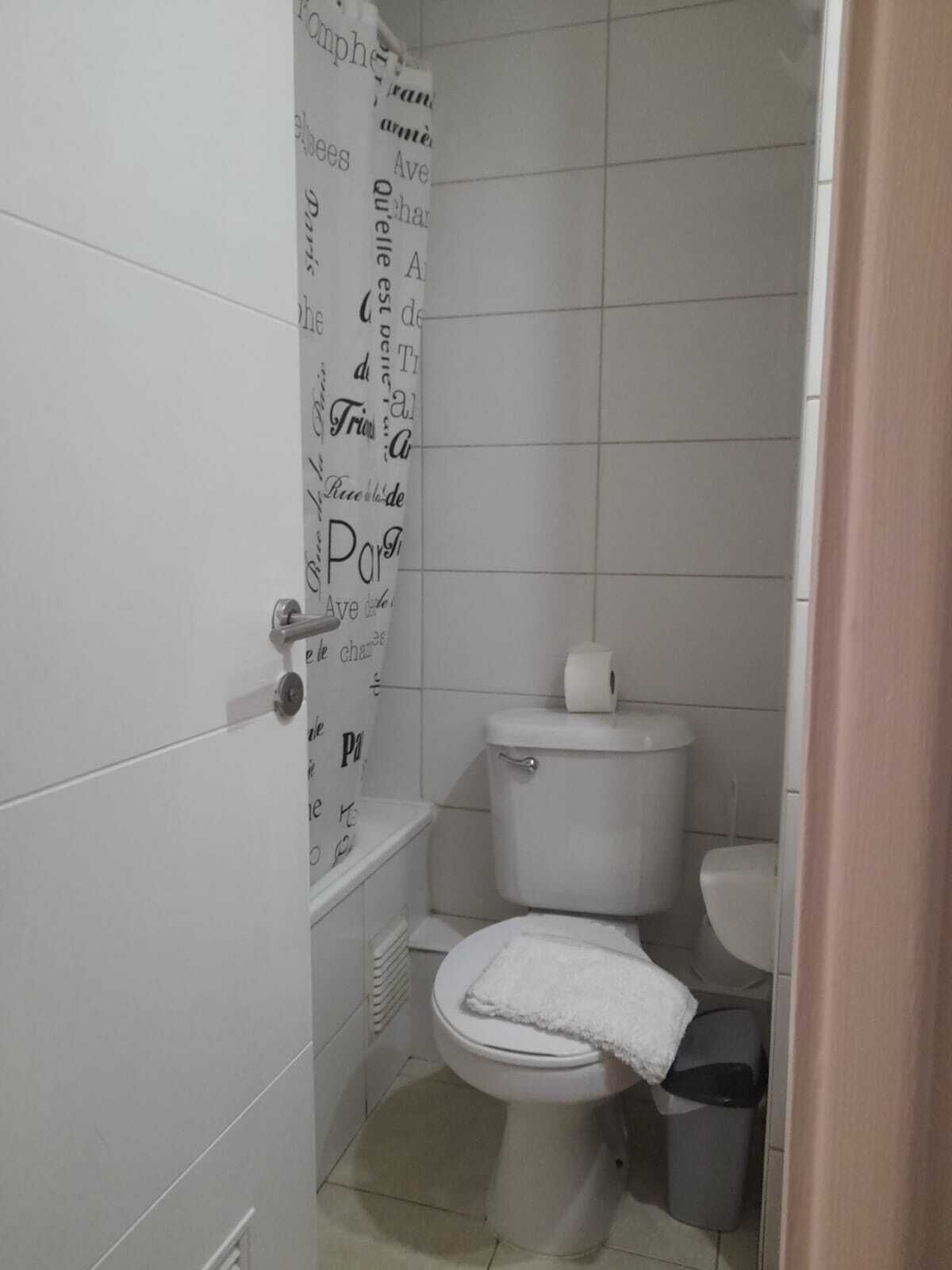 A small, clean bathroom with a toilet, a trash bin, and a shower curtain with text.
