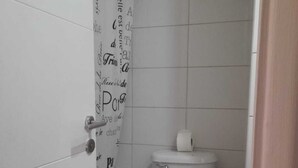 Pieni, siisti kylpyhuone, jossa on wc, roskakori ja tekstillä varustettu suihkuverho.