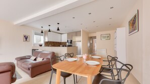 A modern living room with a brown leather sofa, a wooden dining table with chairs, and a kitchen in the background. - Flat for 4 in the centre of Sarzeau (Sarzeau)