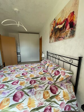 A bedroom with a bed, a painting on the wall, and a ceiling light fixture.