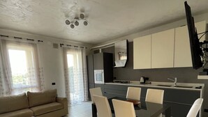 A modern kitchen with a dining area, a sofa, and a TV mounted on the wall.
