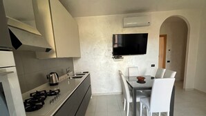 A modern kitchen with a dining area, including a TV mounted on the wall, a gas stove, and a coffee maker.