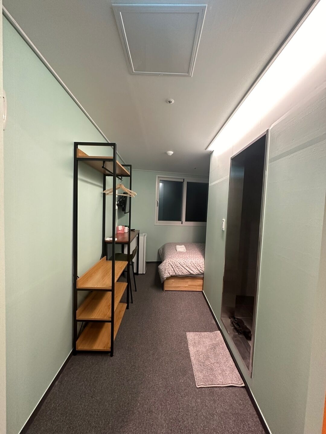 A narrow room with a bunk bed, a desk with a chair, a radiator, and a window.