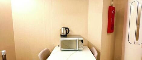 A modern kitchen with a marble countertop, a built-in microwave, a kettle, and a refrigerator.