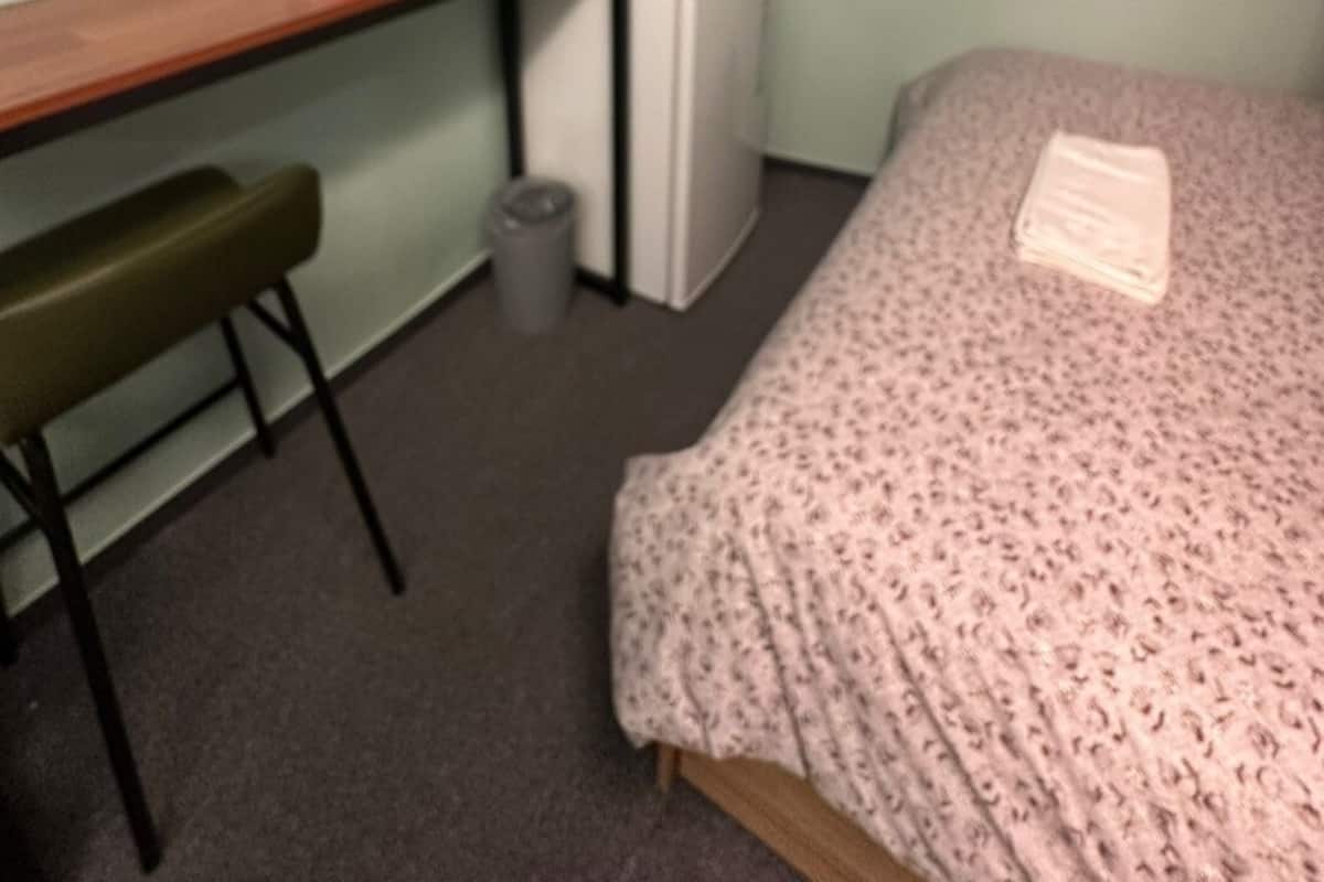 A small room with a bed, a desk, a chair, a television, and a window.