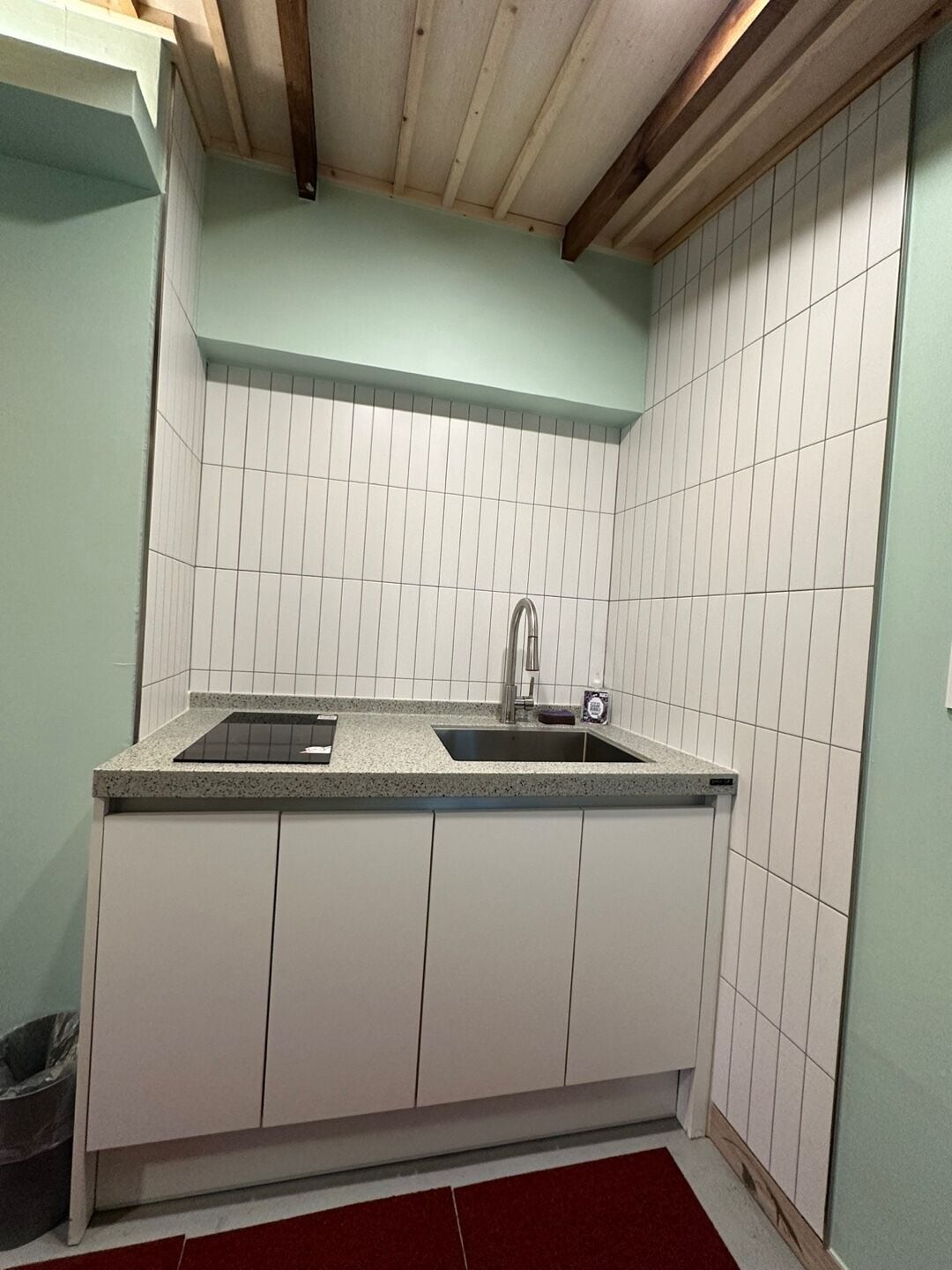A compact kitchen with white cabinets, a granite countertop, and a stainless steel sink.
