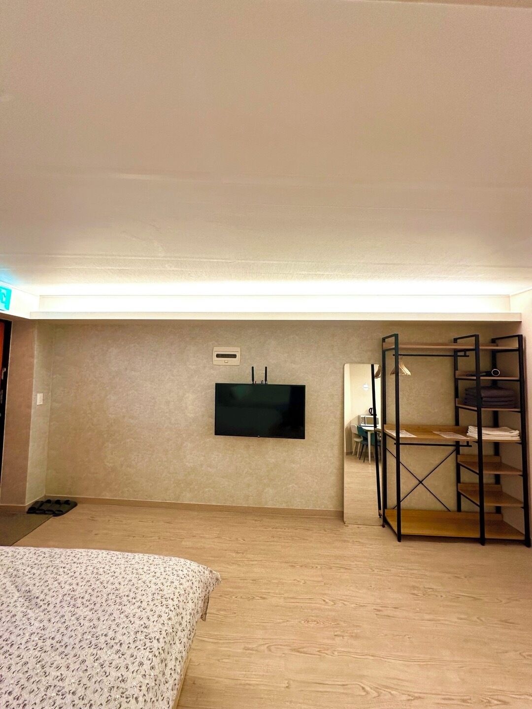 Un dormitorio con una cama, un televisor en la pared, un escritorio con una silla y una estantería.