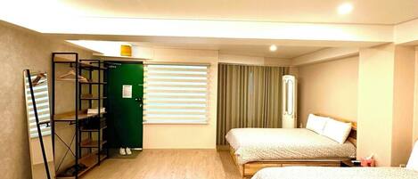 A hotel room with two beds, a wardrobe, a mirror, and a green door.