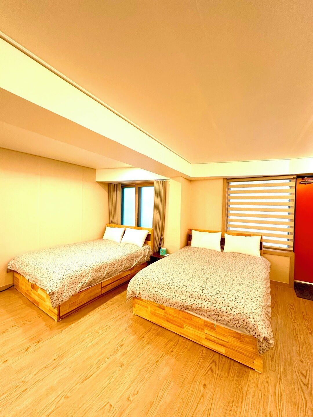A bedroom with two wooden beds, a window with curtains, and a red wall.