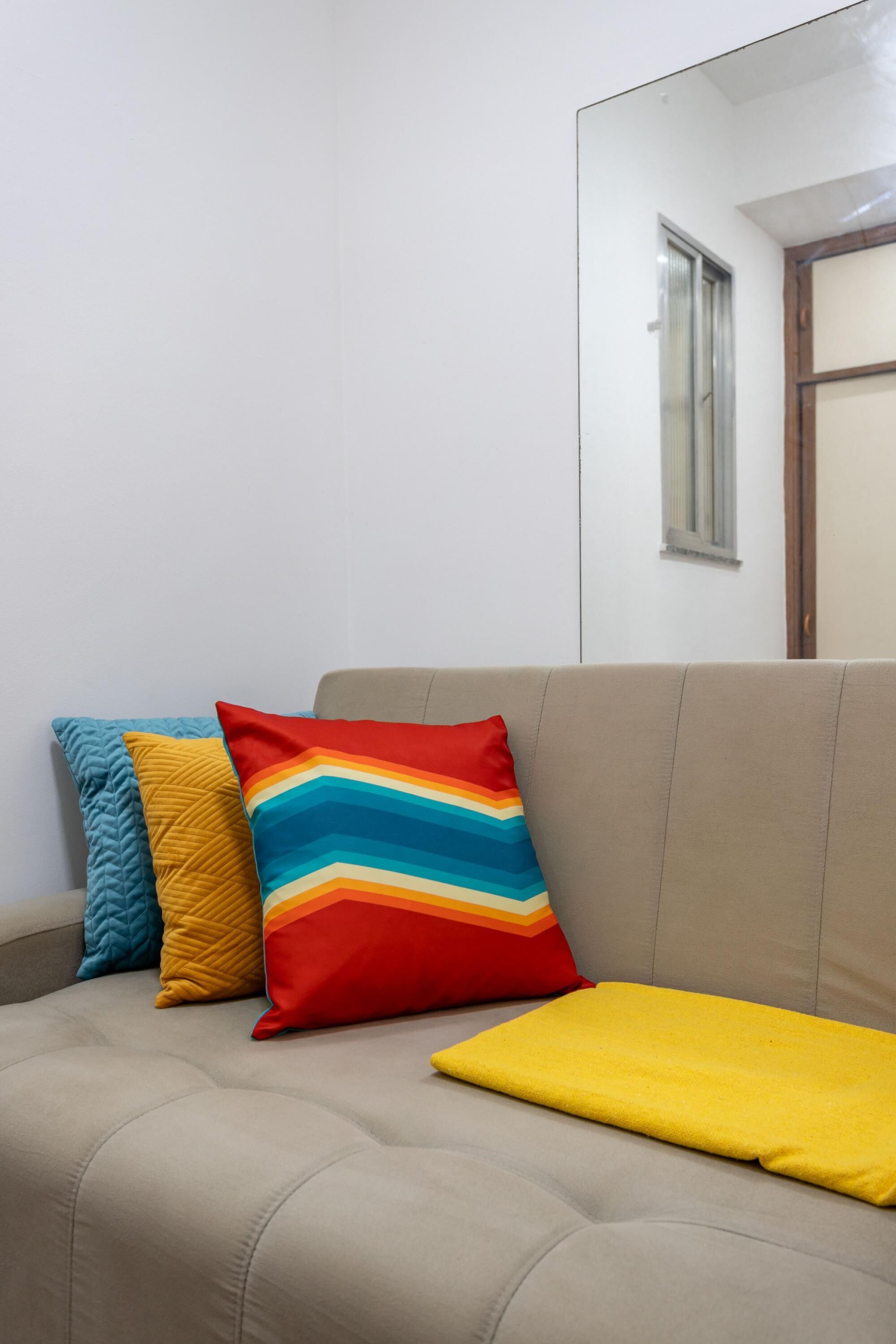 En beige sofa med tre puder i forskellige farver og mønstre.