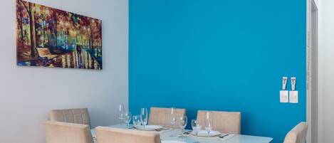 Comedor con mesa blanca para cuatro, sillas color beige, pared de acento azul, piso de madera y una lámpara en el techo.