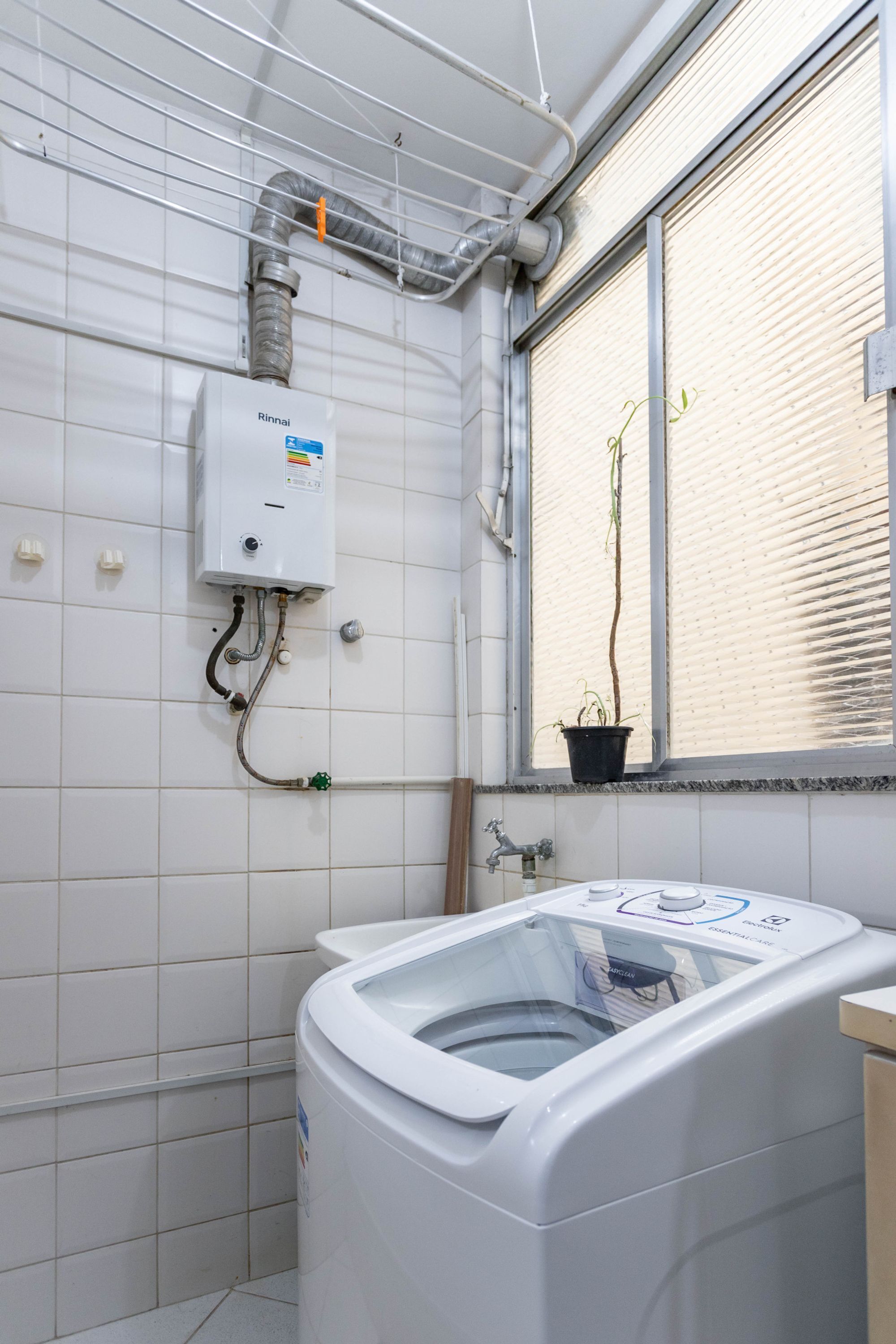 Uma lavanderia com máquina de lavar, aquecedor de água e janela com persianas.