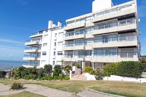 A multi-story building with balconies, a paved entrance, and a view of the sea.