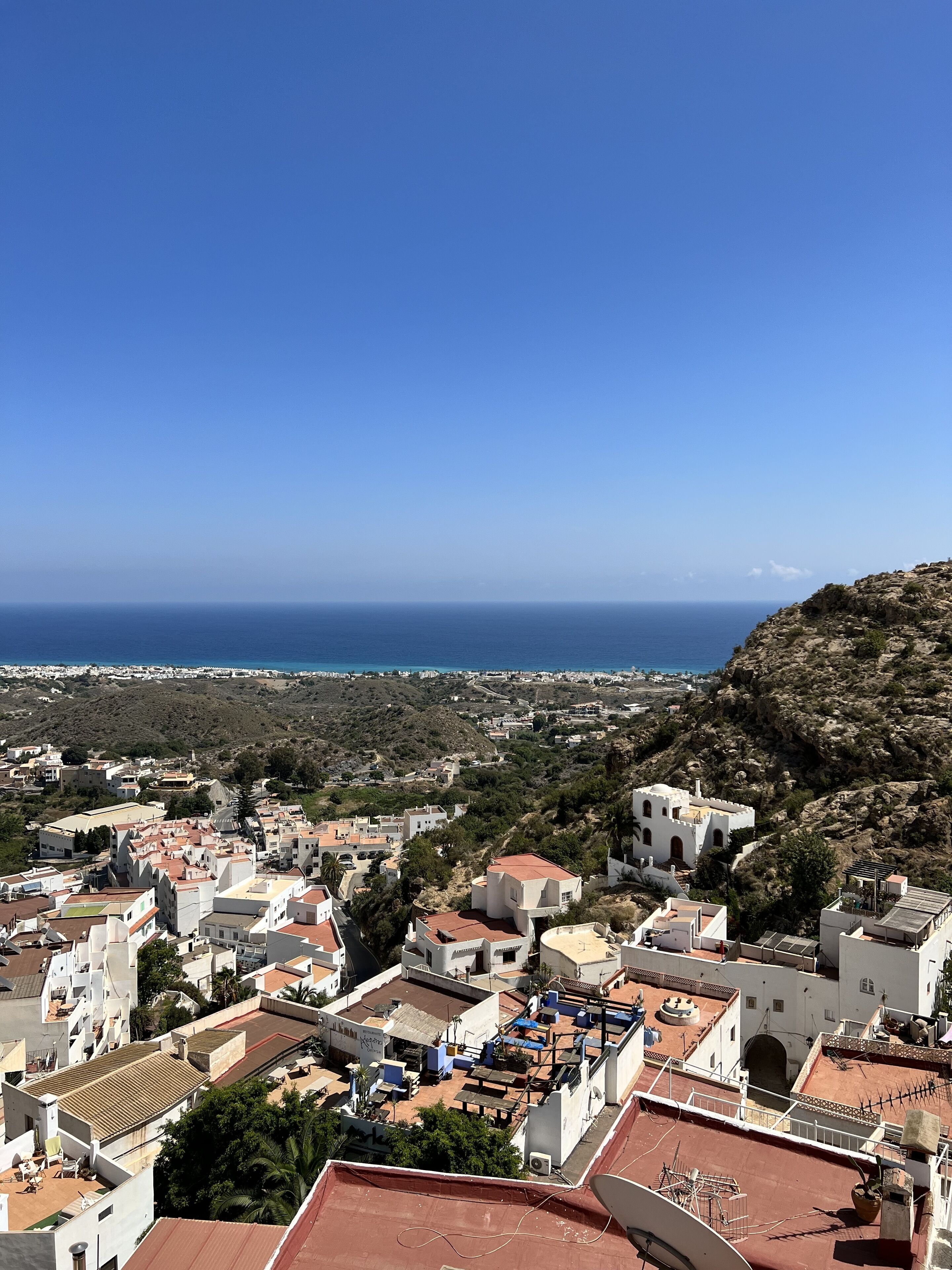 Un pueblo costero con edificios blancos, tejados de tejas rojas y vista al mar.