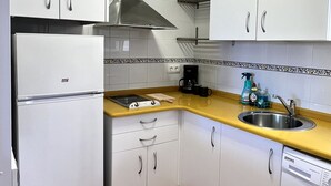 Una cocina compacta con armarios blancos, un lavamanos de acero inoxidable, una lavadora y una cafetera.