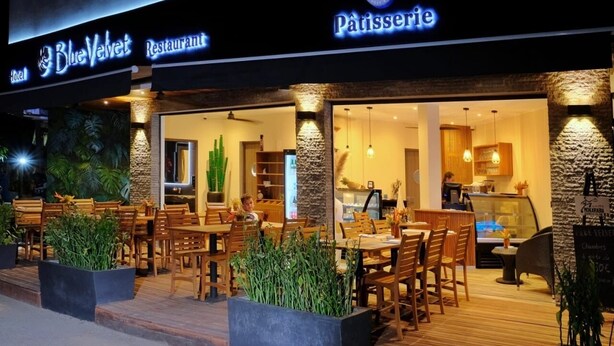 A restaurant with outdoor seating, a sign reading "Blue Velvet Restaurant," and a visible interior with wooden furniture and a stone column. - BLUE VELVET (Nosy Be)