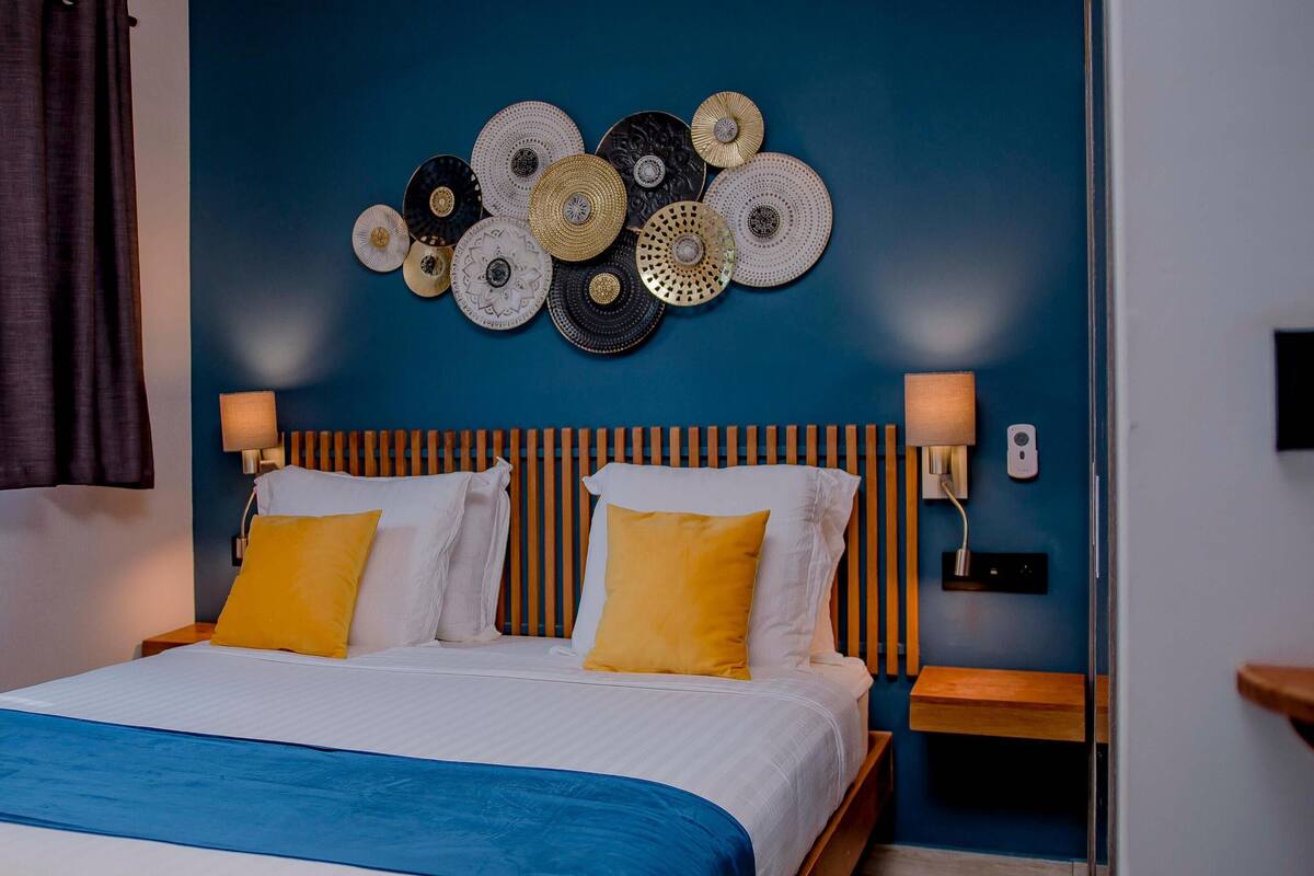 A hotel room with a bed, two bedside lamps, a wall-mounted light fixture, and a decorative wall art piece.