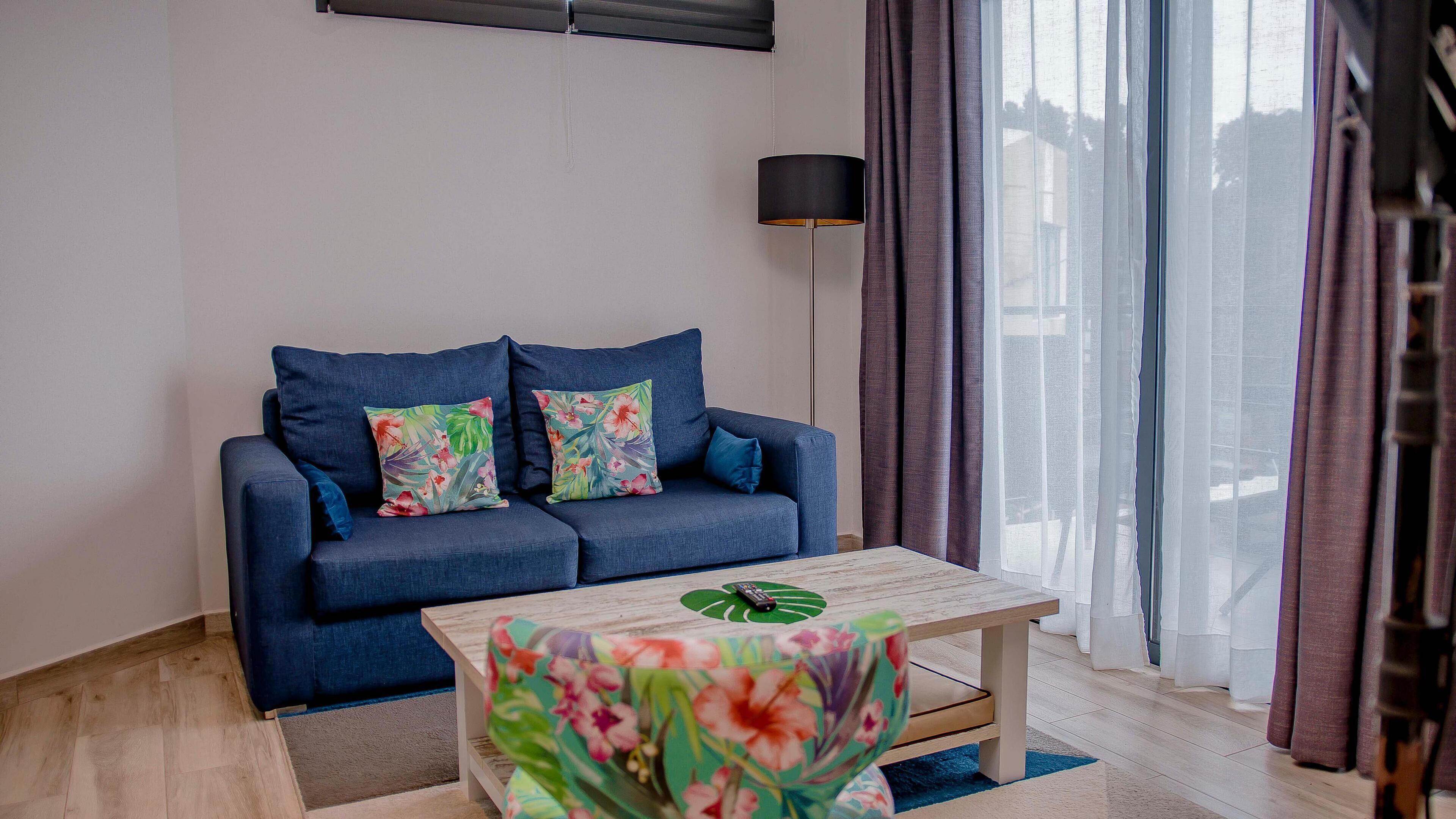 Un salon moderne avec un canapé bleu, des coussins à motifs floraux, une table basse en bois et un lampadaire.
