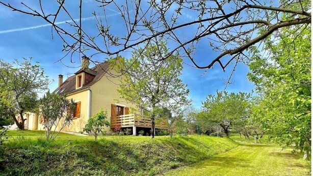 A house with a wooden deck, surrounded by lush greenery and trees. - Le Gîte Isabel en Dordogne, Près de Sarlat (Saint-Crépin-et-Carlucet)
