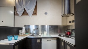 A compact kitchen with a stainless steel sink, a dishwasher, and a red kettle.