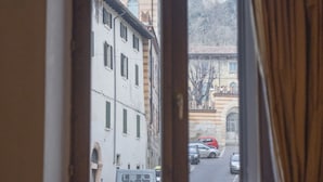 A room with a window overlooking a street with buildings and parked cars.